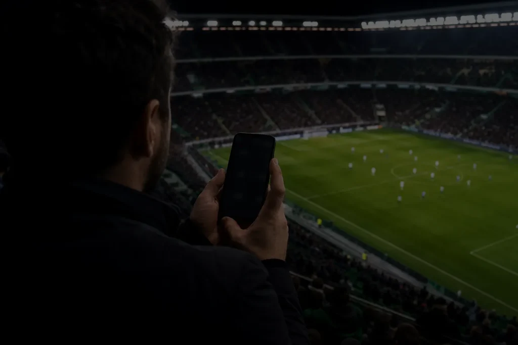 Pessoa usando o celular durante uma partida de futebol no estádio